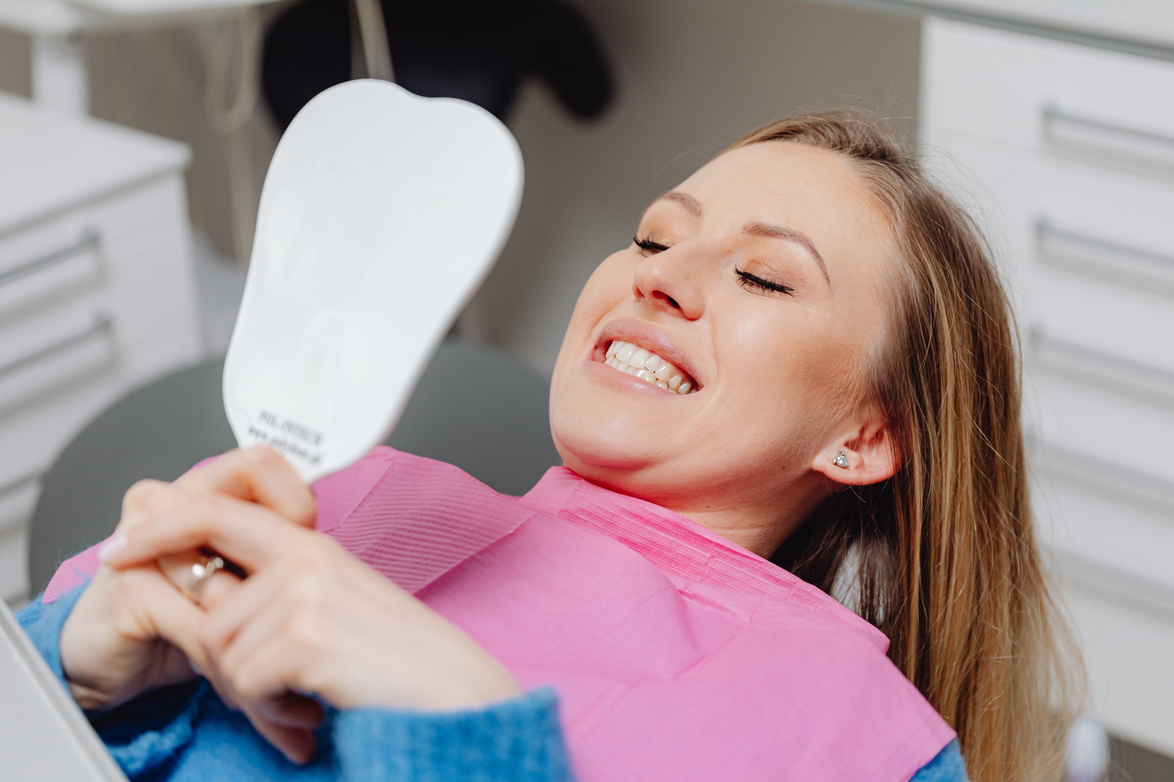 A patient checking her smile in a hand mirror after treatment
